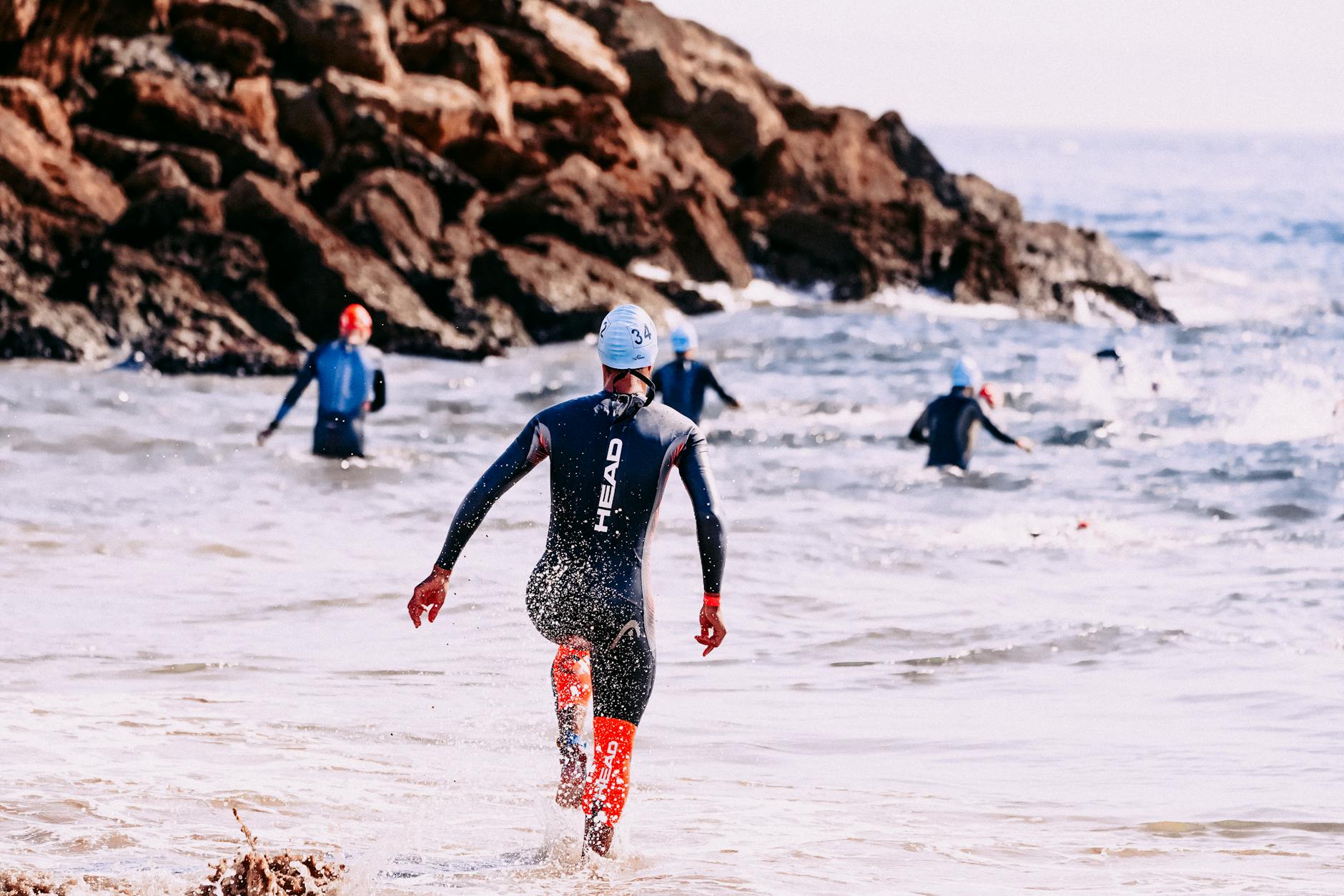 unrecognizable sportsmen in wet suits swimming in foamy ocean